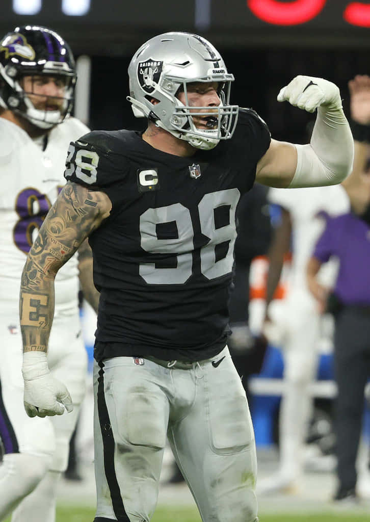 Maxx Crosby Flexing Against Baltimore Ravens Background