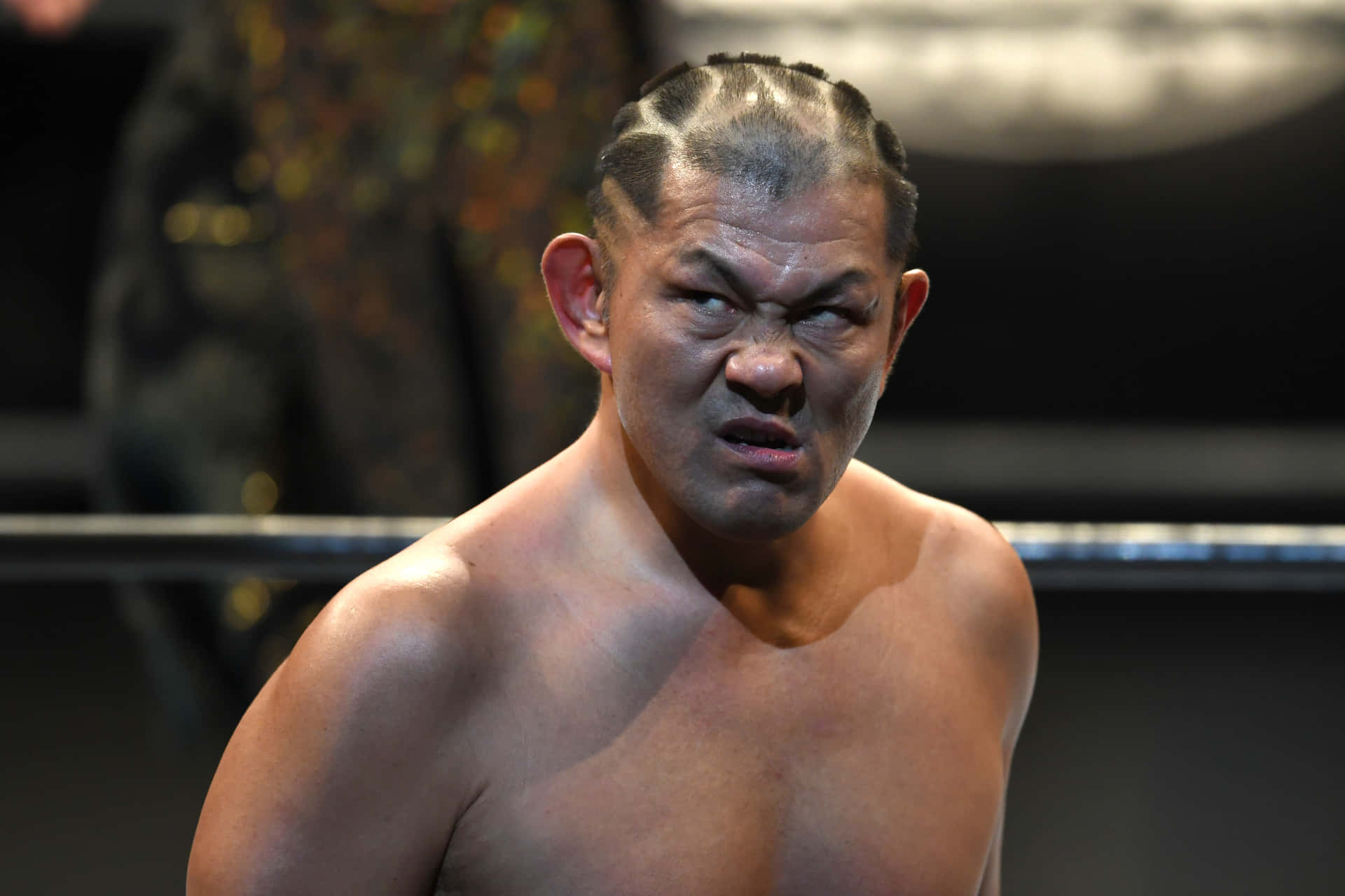 Minoru Suzuki Showcasing His Iconic Angry Expression In The Ring Background