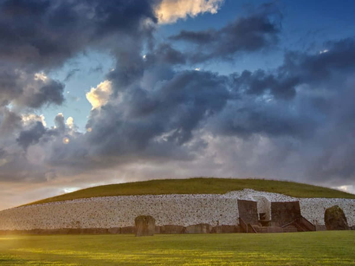 Newgrange With Stormy Clouds And Sunset Lighting Background