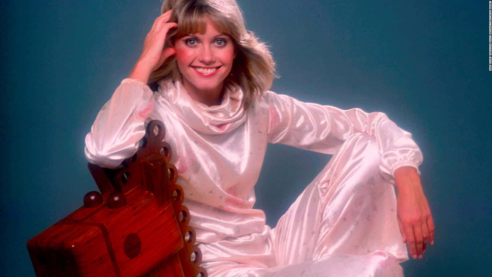 Olivia Newton John Sitting On Wooden Chair Background