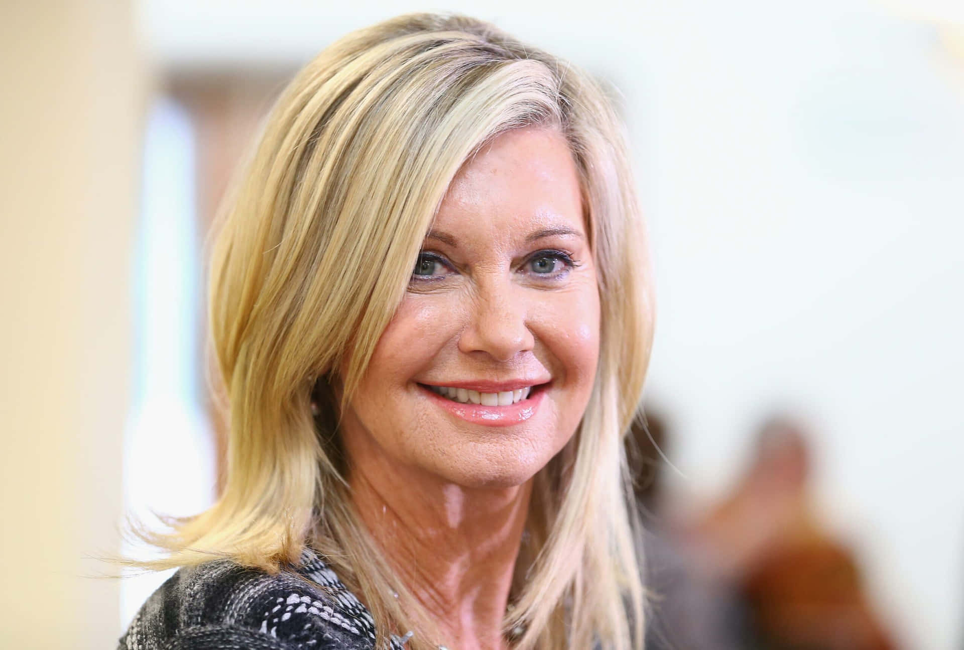 Olivia Newton John Smiling Against Blurry Background Background