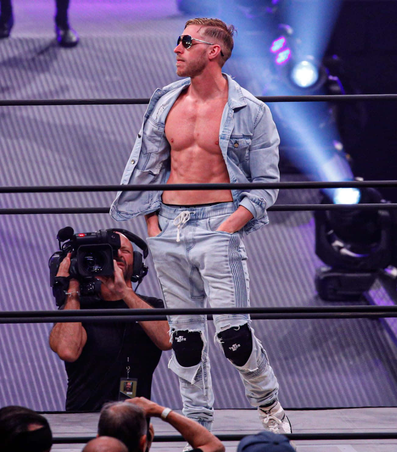 Orange Cassidy In Deep Thought Beside A Cameraman Background