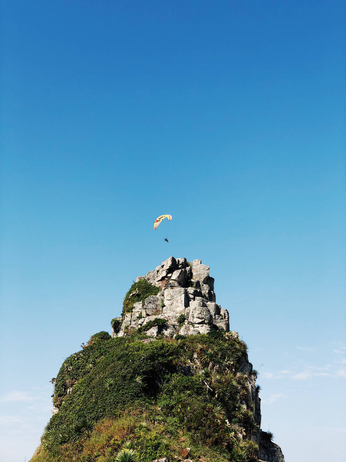 Paragliding Above Pointed Rock Cliff Background