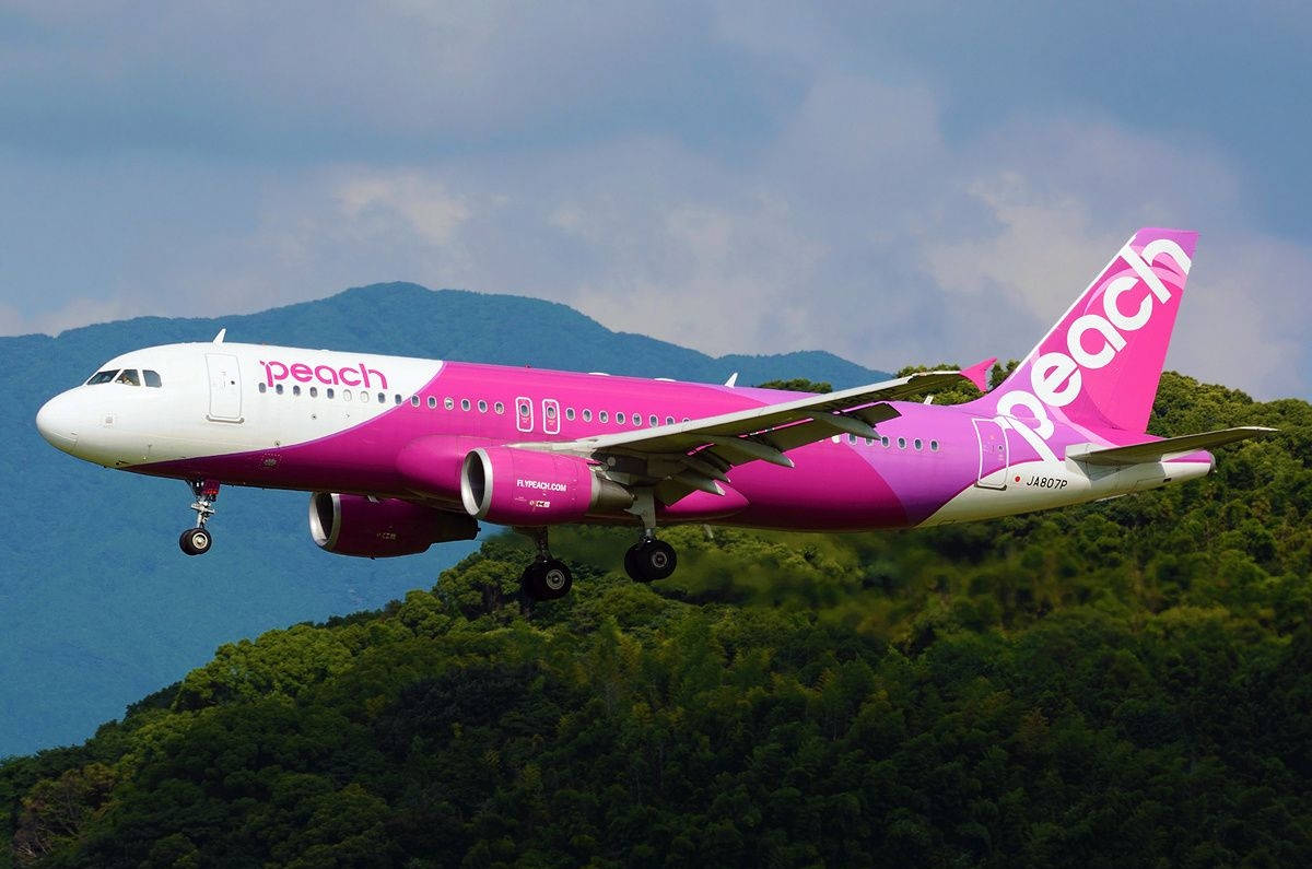 Peach Aviation Flying Over Green Mountain Background