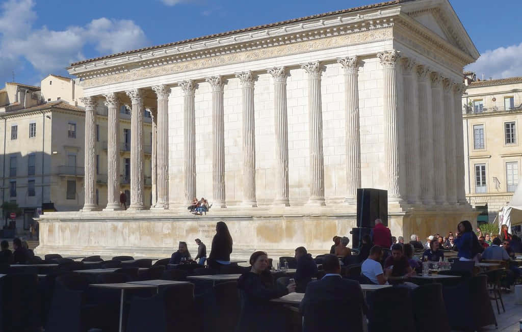 People Seated Around Maison Carrée Background