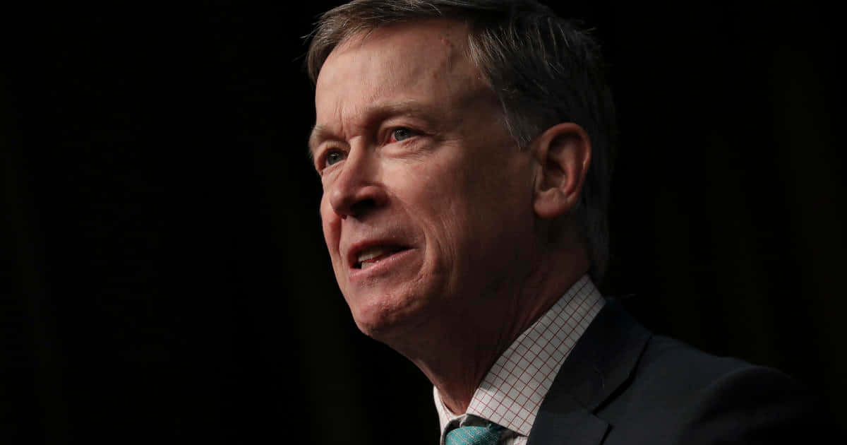 Permanent Governor John Hickenlooper Poses Against A Black Backdrop Background