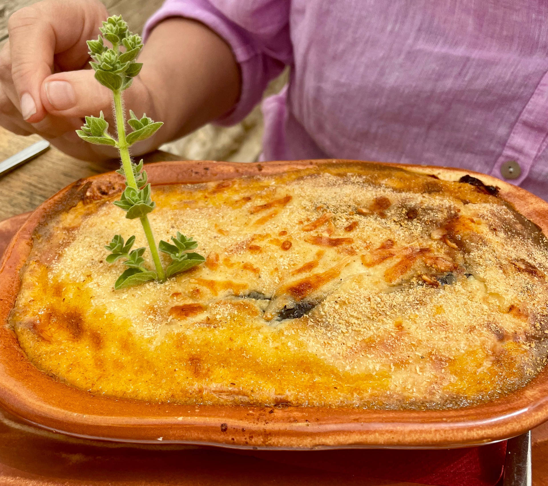 Person's Hand Garnishing A Baked Moussaka Background