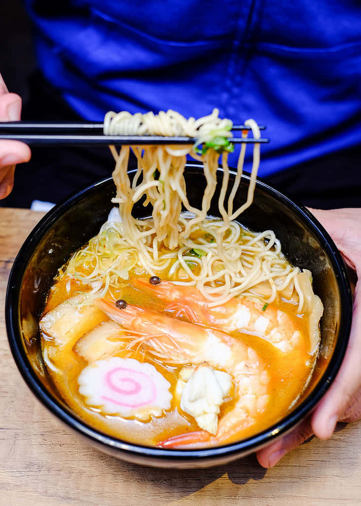 Person's Hand Grabbing Ramen Using Chopsticks Background