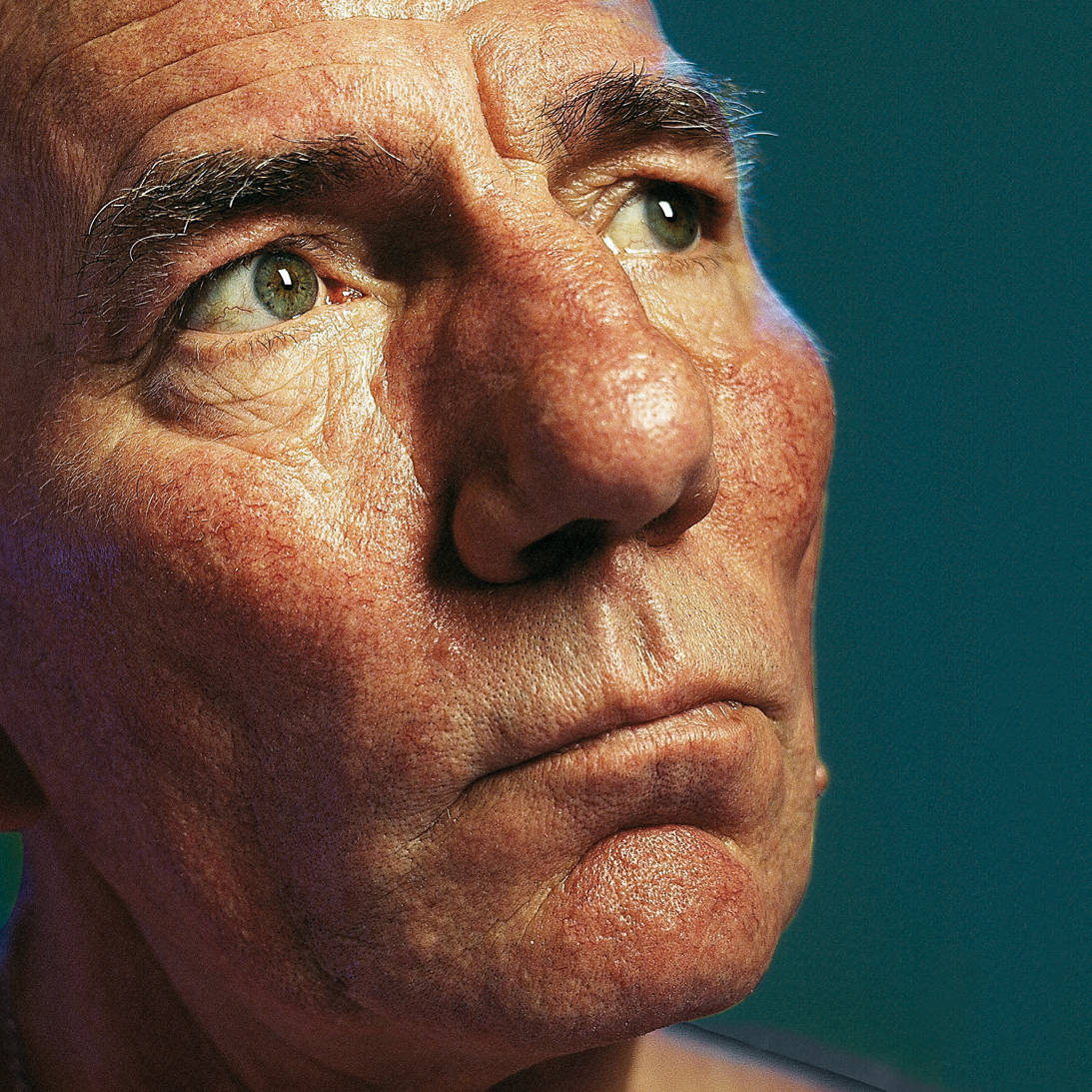 Pete Postlethwaite Looking Up With Green Eyes Background