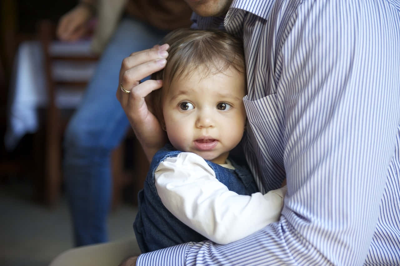 Photo Of A Tangible Baby Being Hug By An Older Person Wearing Striped Long Sleeve Background