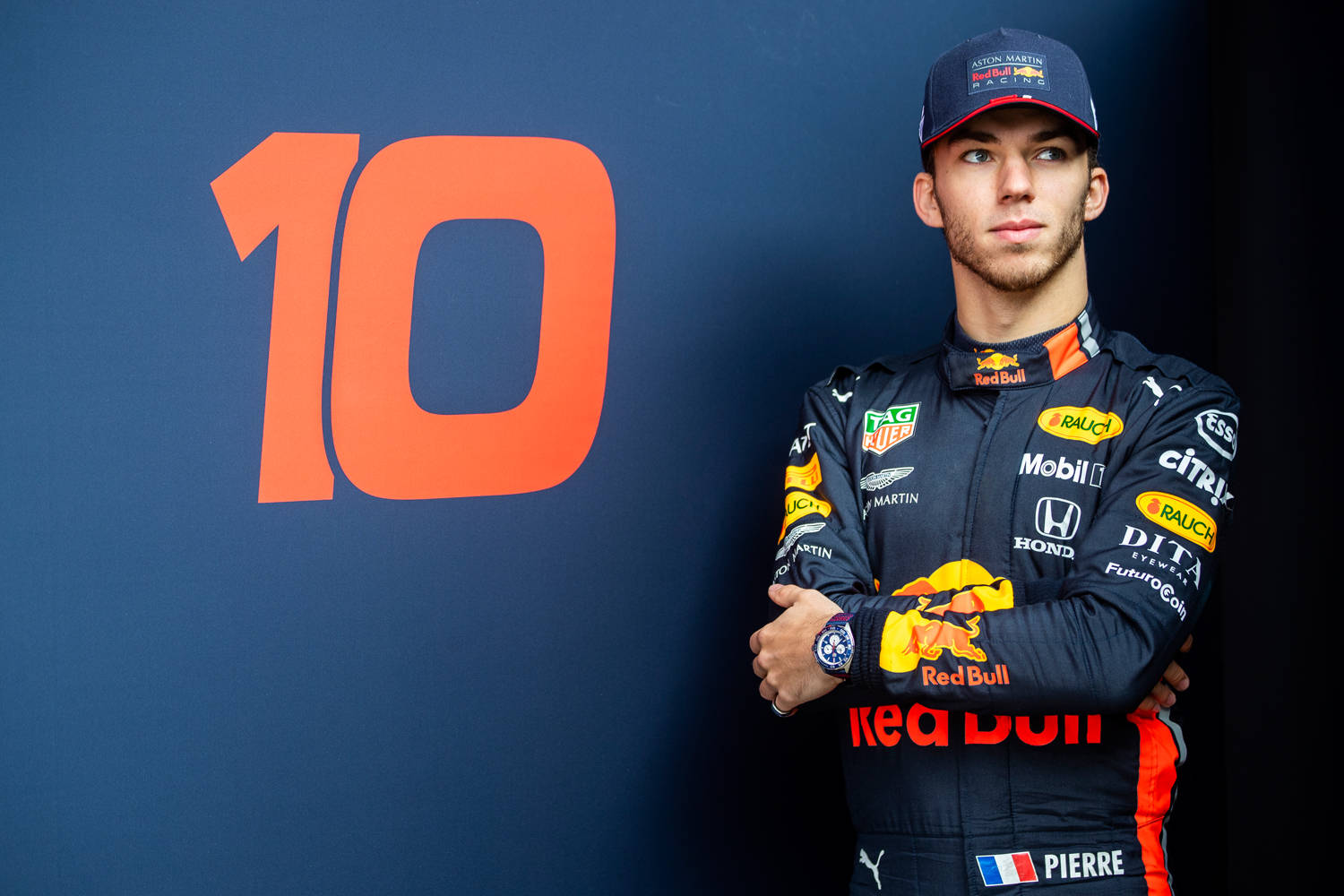 Pierre Gasly Striking A Pose Beside His Race Car Background