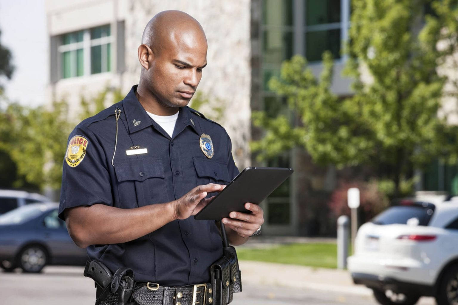 Police Officer Accessing Information On Handheld Device In The Field Background