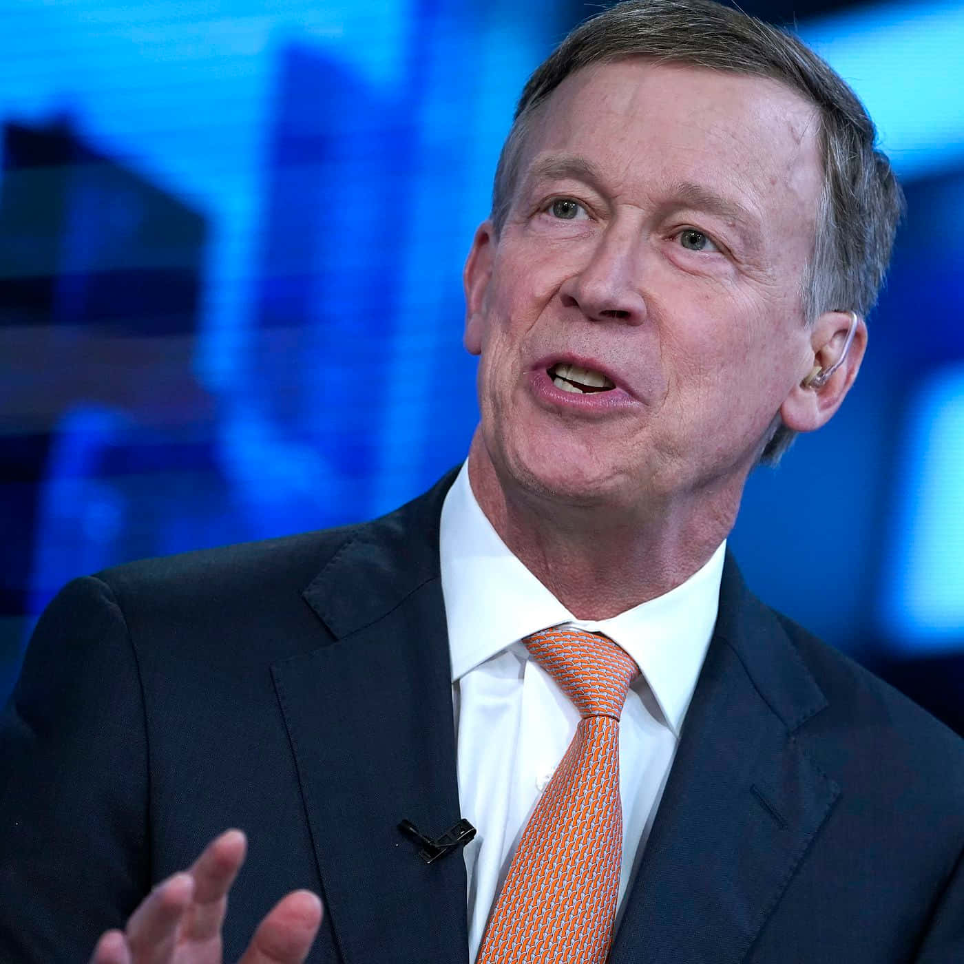 Portrait Of John Hickenlooper With A Blue Backdrop Background