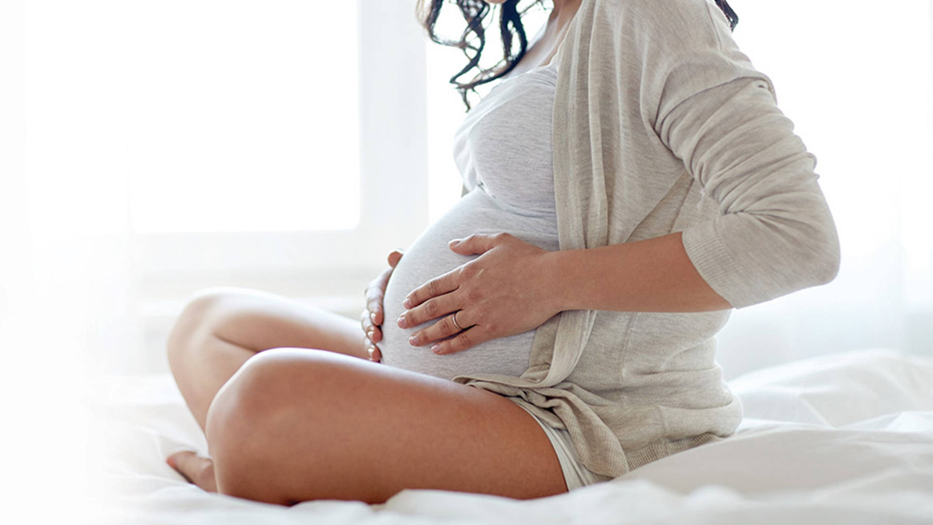 Pregnant Belly Massaging On White Bed Background