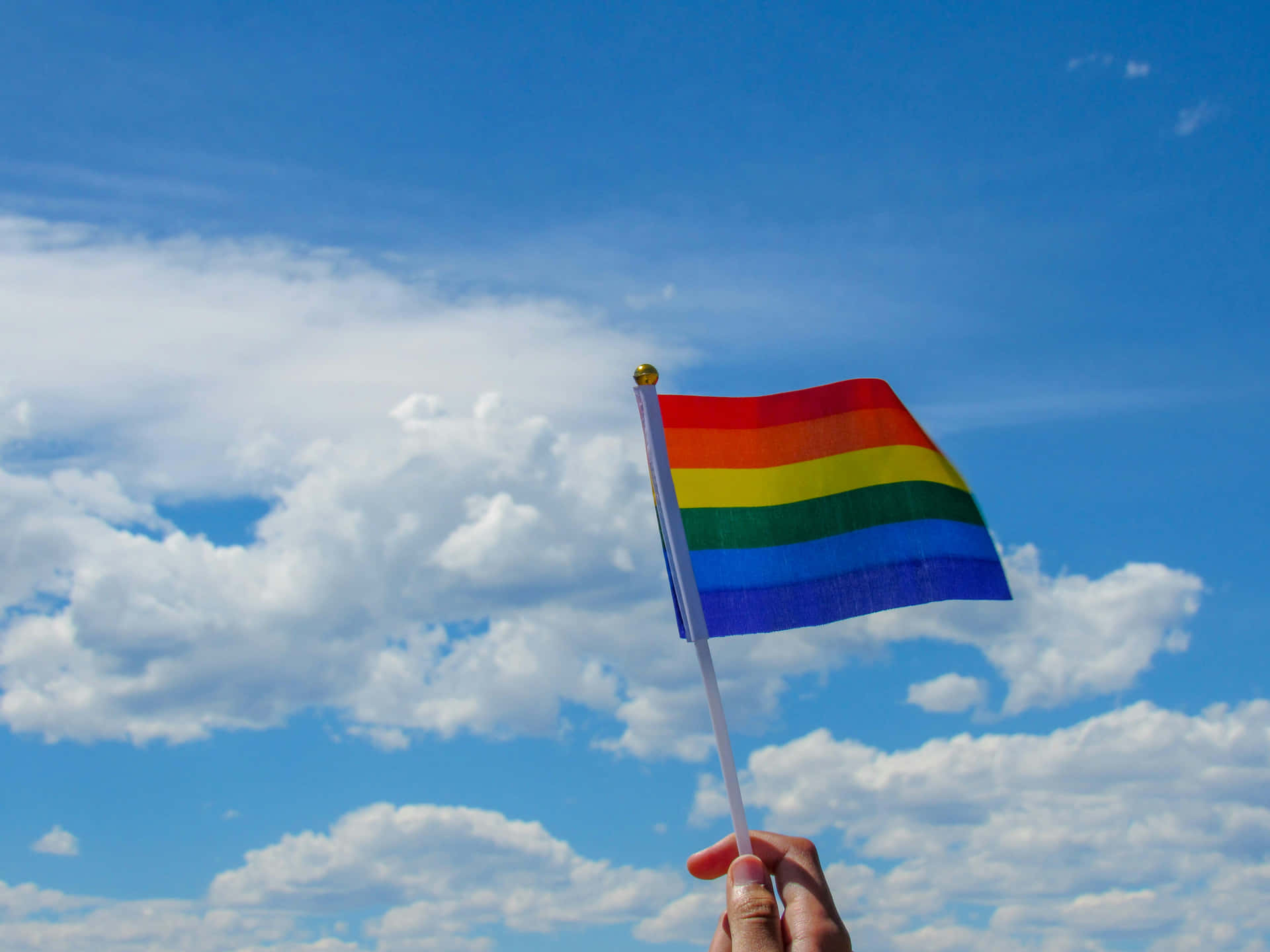 Pride_ Flag_ Waving_ Against_ Blue_ Sky Background