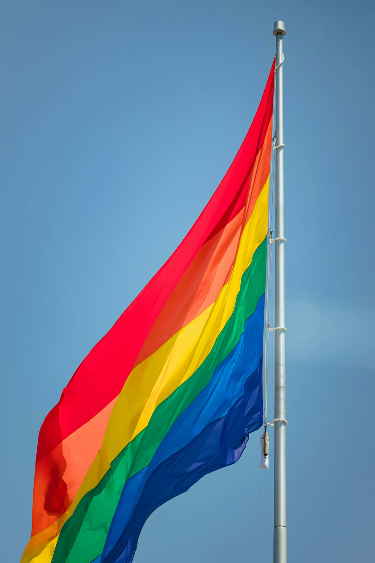 Pride_ Flag_ Waving_ Against_ Blue_ Sky Background