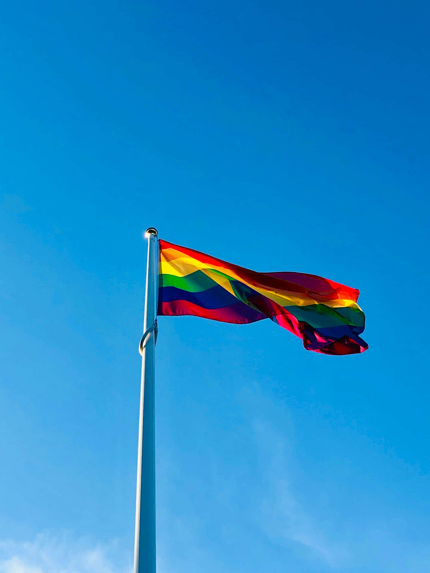 Pride Flag Waving Against Blue Sky Background