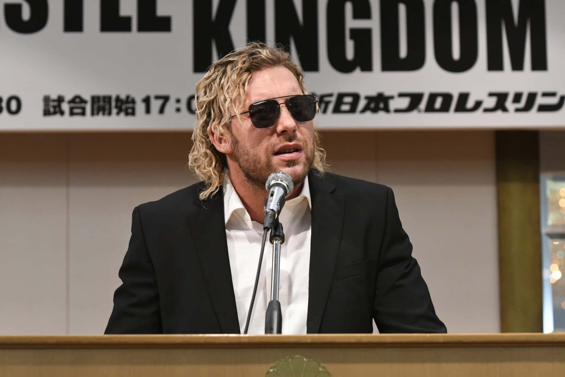 Pro Wrestler Kenny Omega Looking Dashing In A Suit And Sunglasses. Background