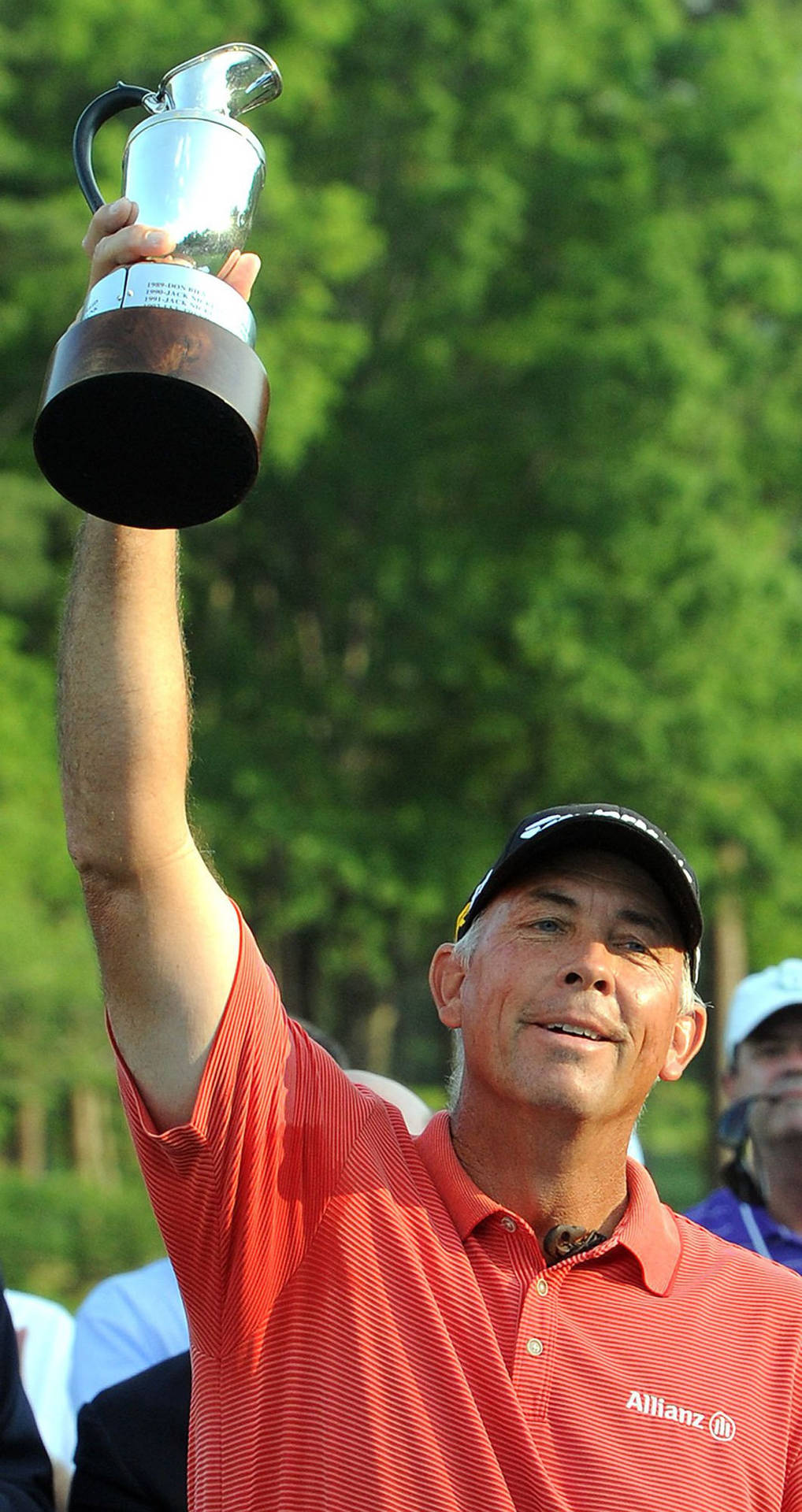 Professional Golfer Tom Lehman Victorious With Trophy Overhead Background