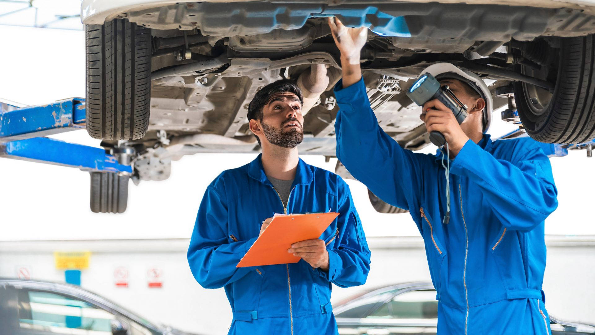 Proficient Mechanical Engineer Technician Inspecting A Car Background