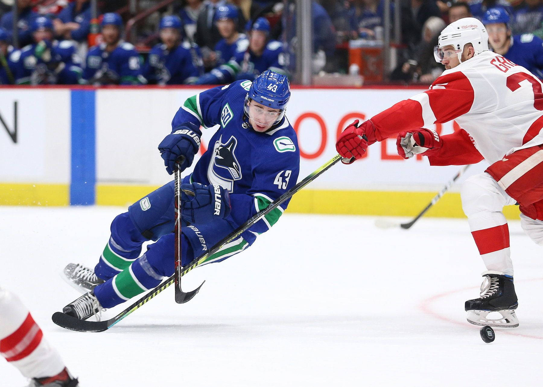 Quinn Hughes Dribbling Hockey Puck Against Player From Detroit Red Wings Background