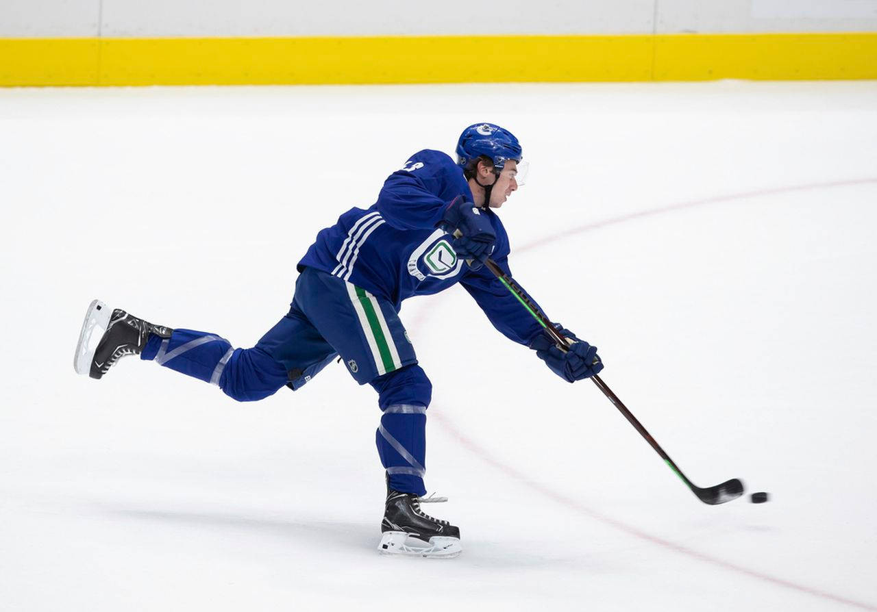 Quinn Hughes Dribbling Hockey Puck With Left Leg Raised During Game Background