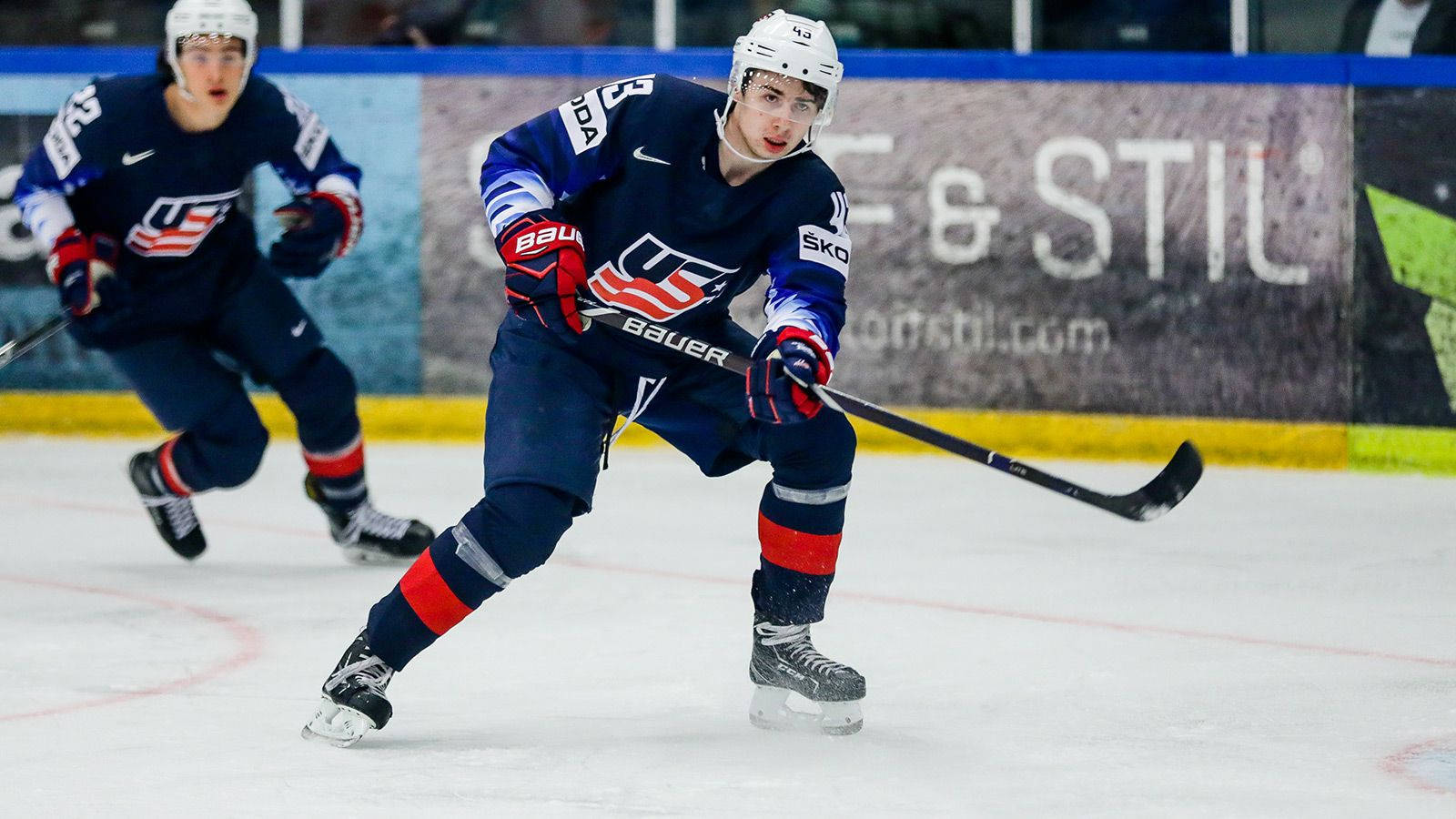 Quinn Hughes Leaning Forward And Holding Hockey Stick To The Left Background