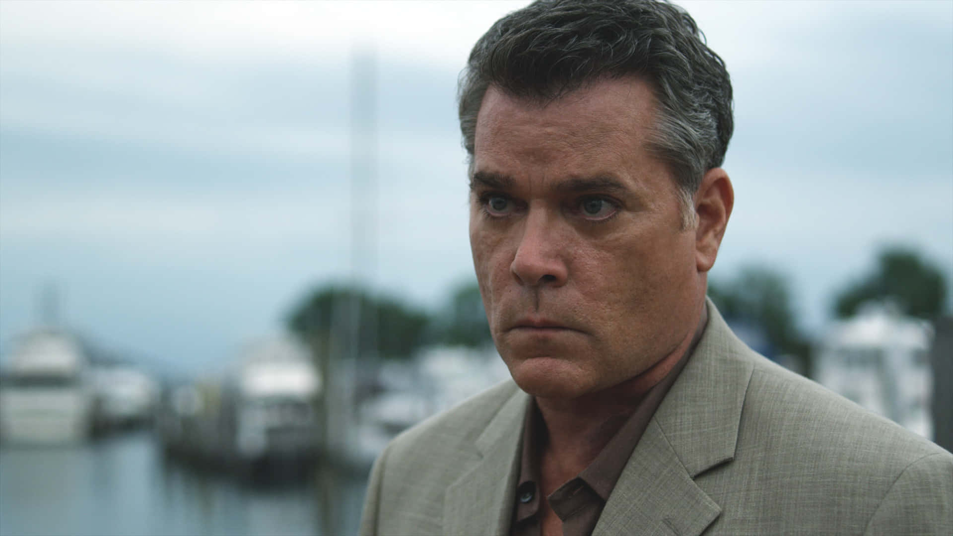 Ray Liotta Looking Seriously While Donning A Sleek Black Suit Background