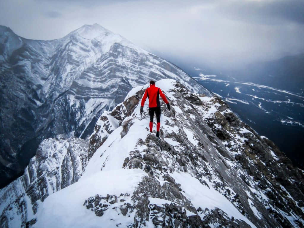 Resilient Man In Red Climbing A Mountain Alone Background