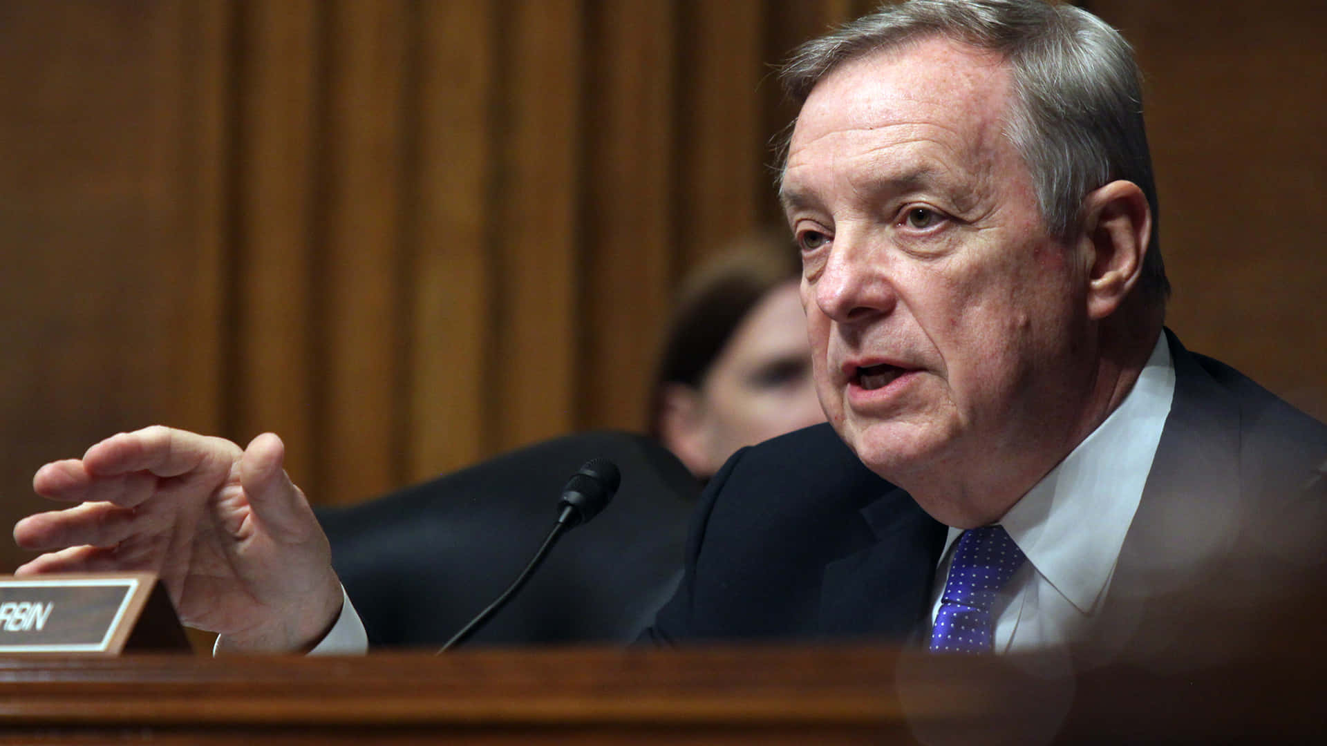 Richard Durbin Talking Into A Microphone Background