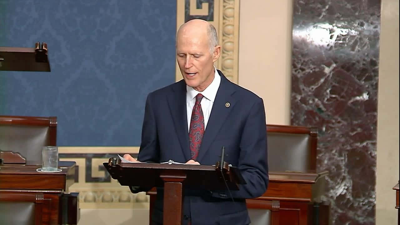 Rick Scott Speaks From A Podium Background