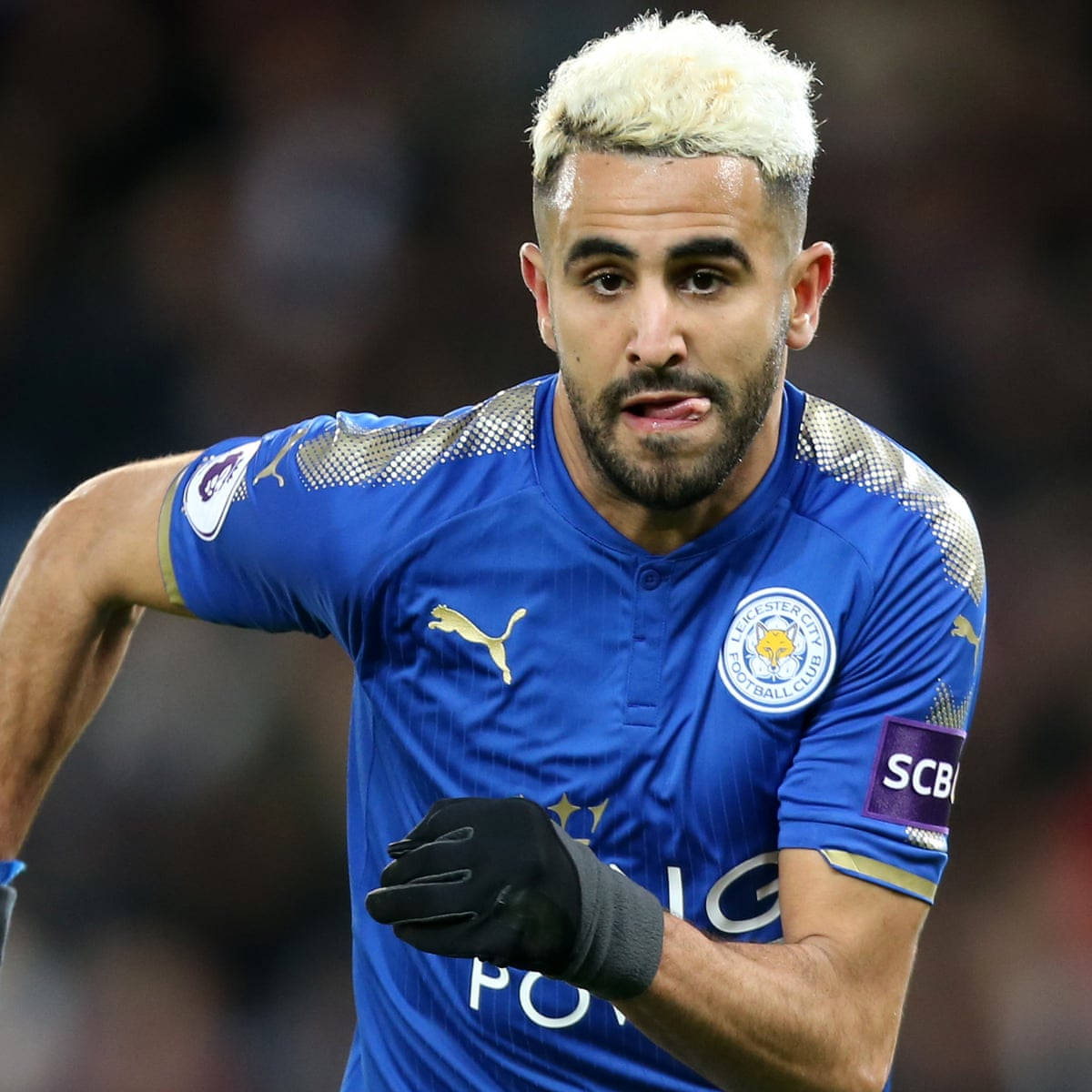 Riyad Mahrez With A Playful Expression On The Field Background