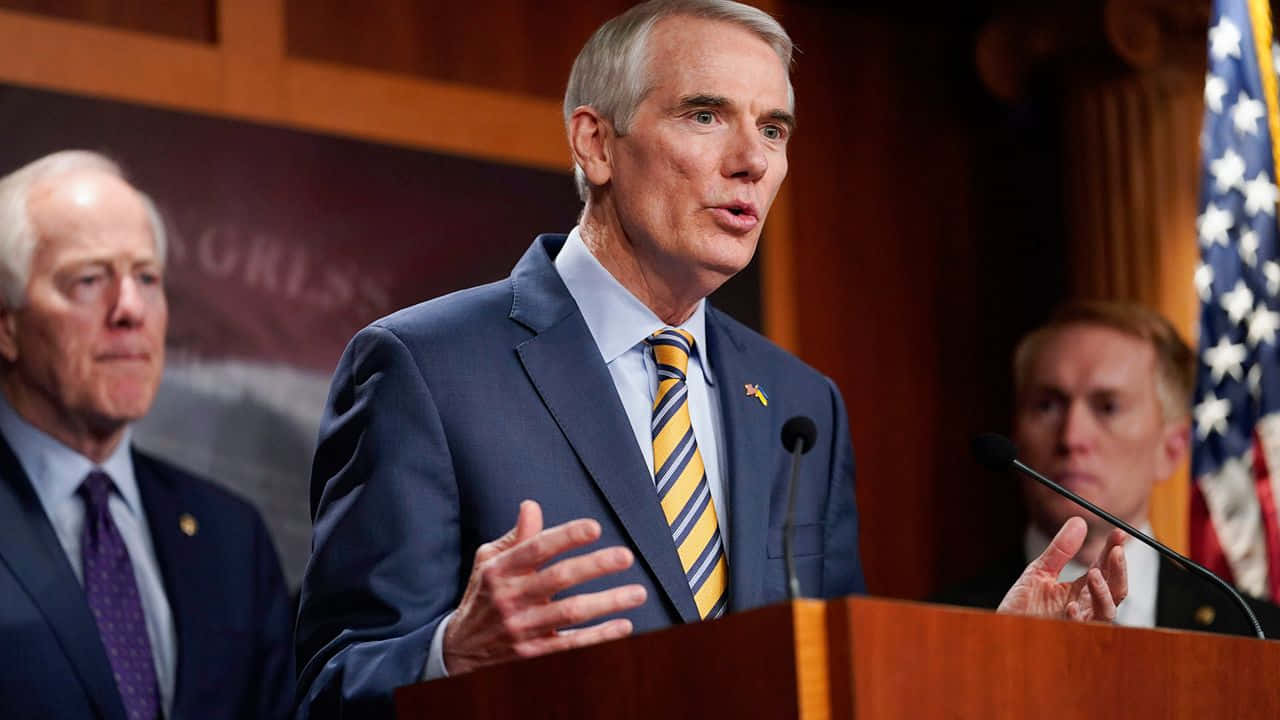 Rob Portman Speaking Two Men Behind Him Background