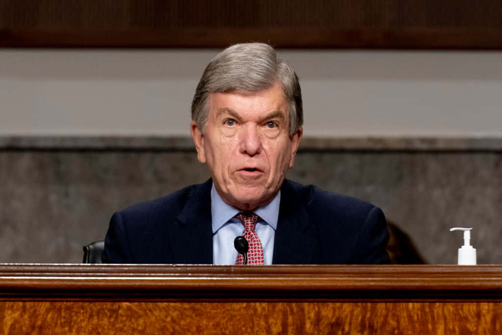 Roy Blunt Thoughtfully Observing From Behind A Ledge Background