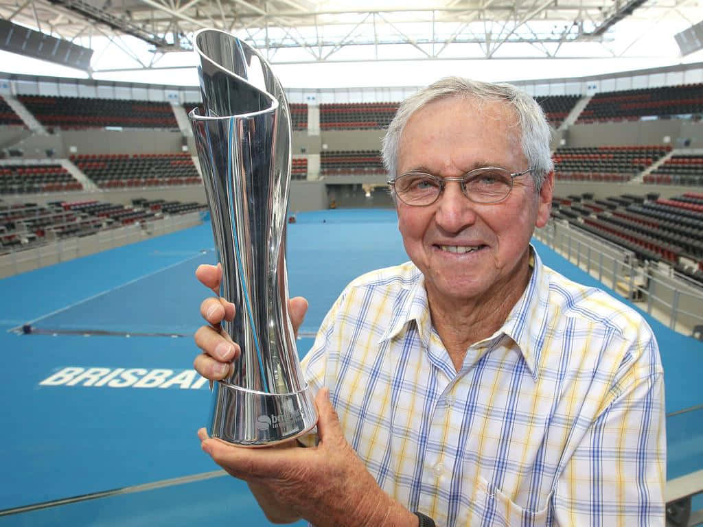 Roy Emerson Holding Trophyat Brisbane Tennis Court Background