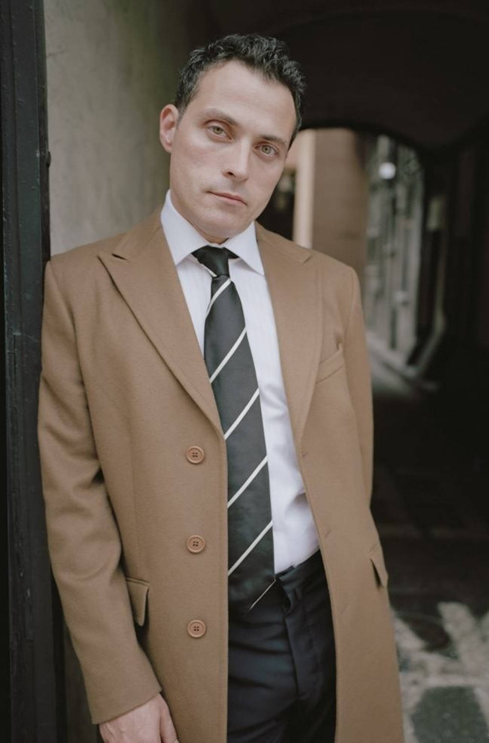 Rufus Sewell In Brown Coat And Striped Tie Background