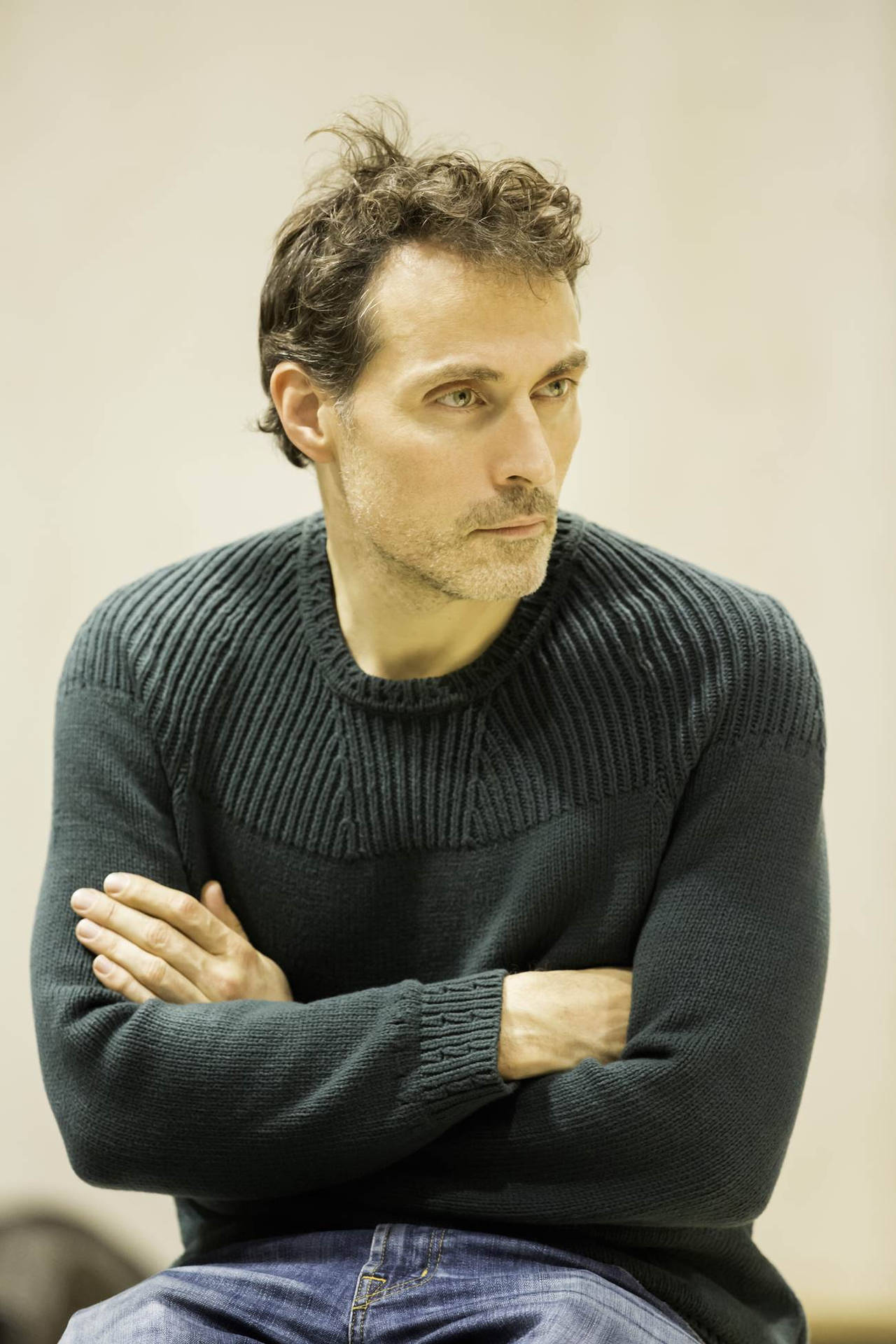 Rufus Sewell Posing With Crossed Arms In Black Sweater Background