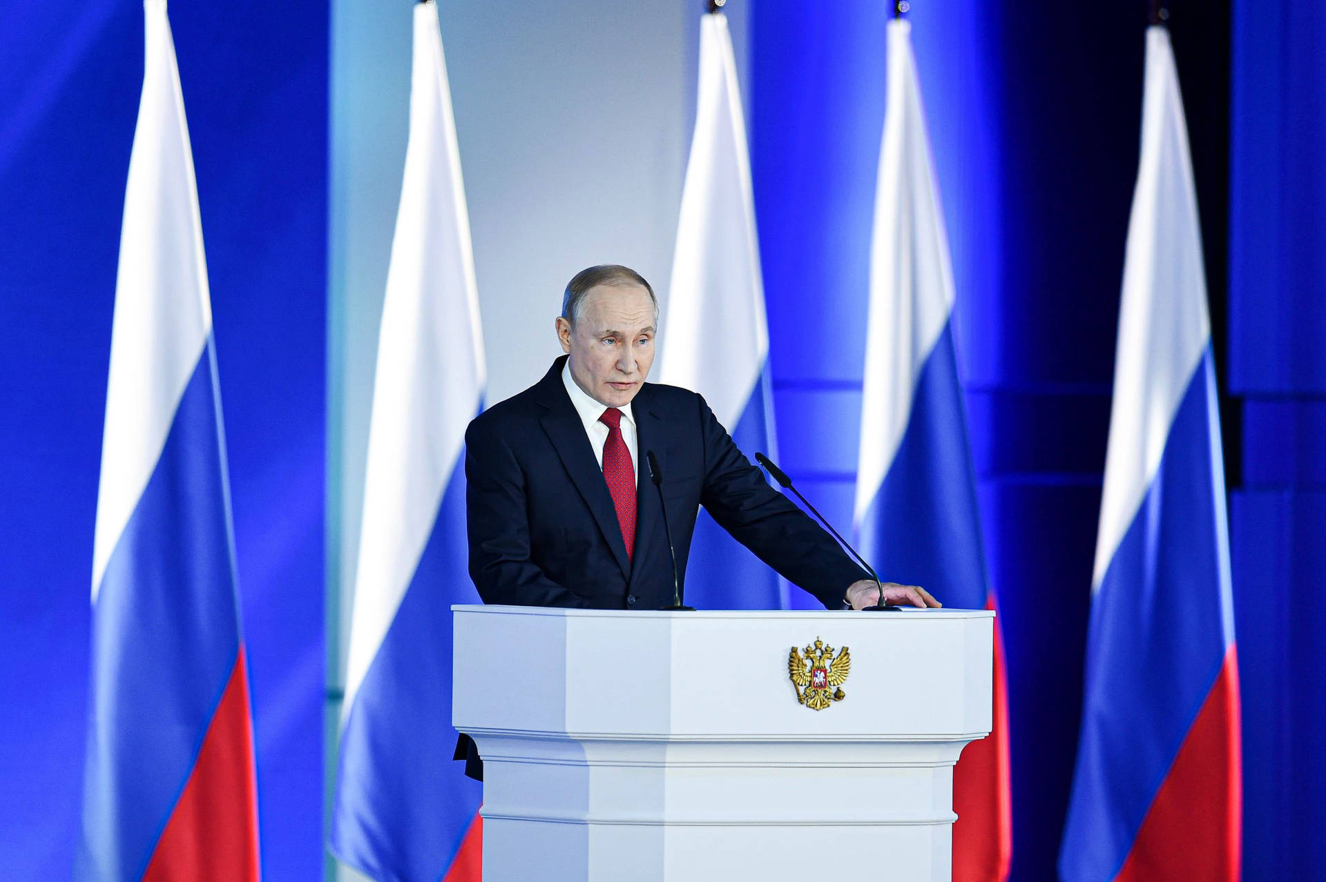 Russian President Vladimir Putin Standing Proudly Before Five Flags