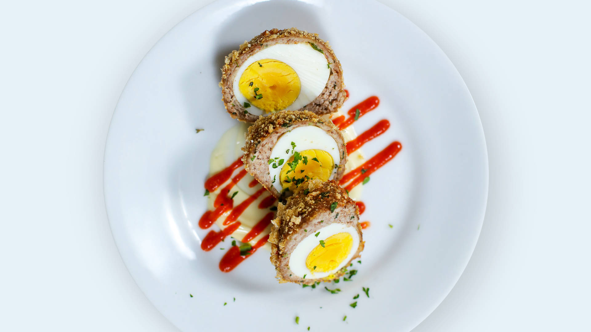 Scotch Eggs Dish With Red Sauce And Herbs