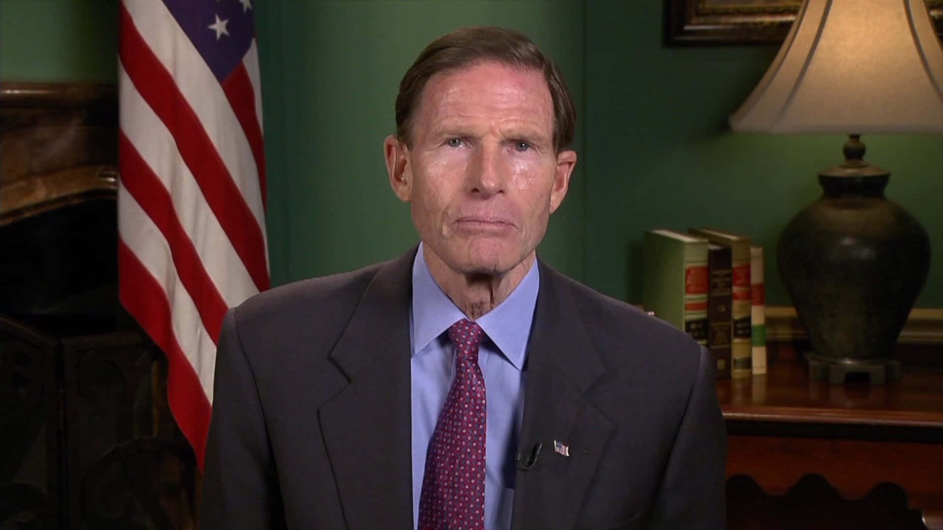 Senator Richard Blumenthal Posed Against A Green Backdrop And An American Flag