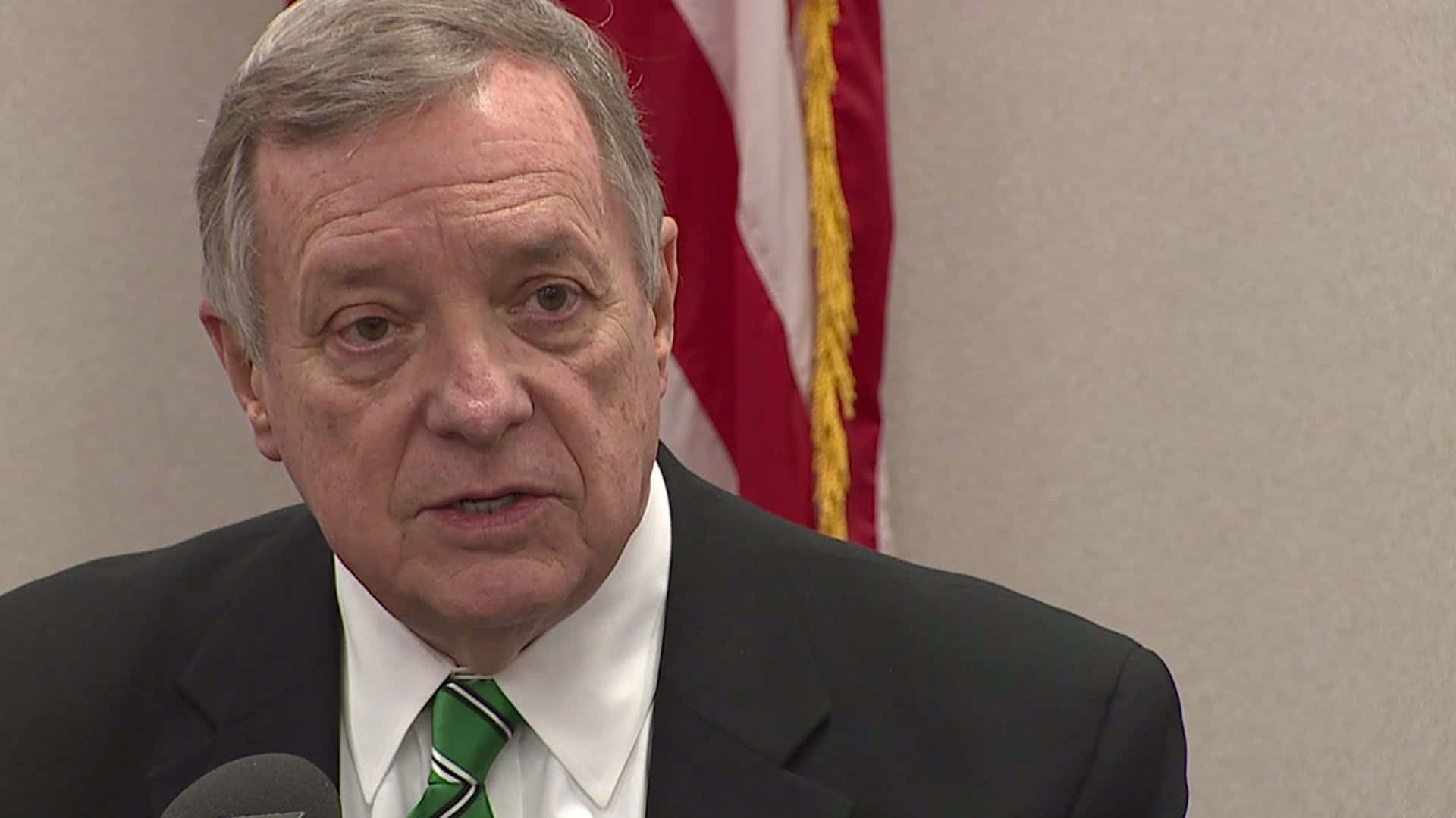 Senator Richard Durbin Delivering A Speech Into A Microphone. Background