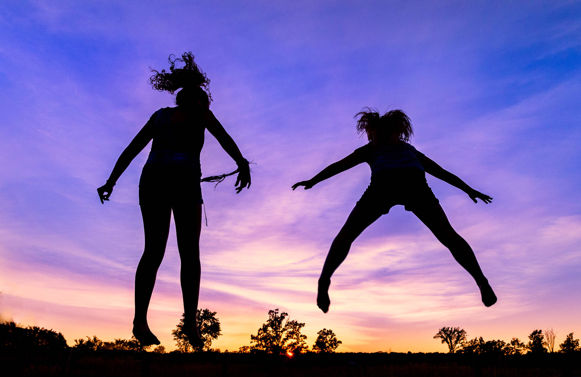 Silhouetted Girls Jumping From A Trampoline