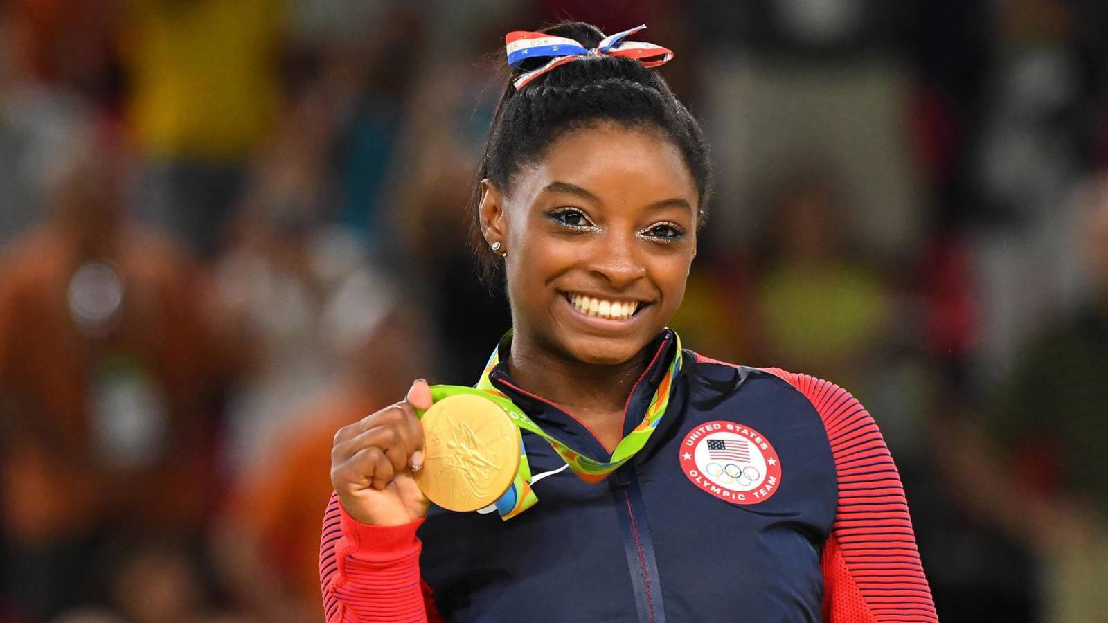 Simone Biles Holding A Gold Medal And Smiling Background