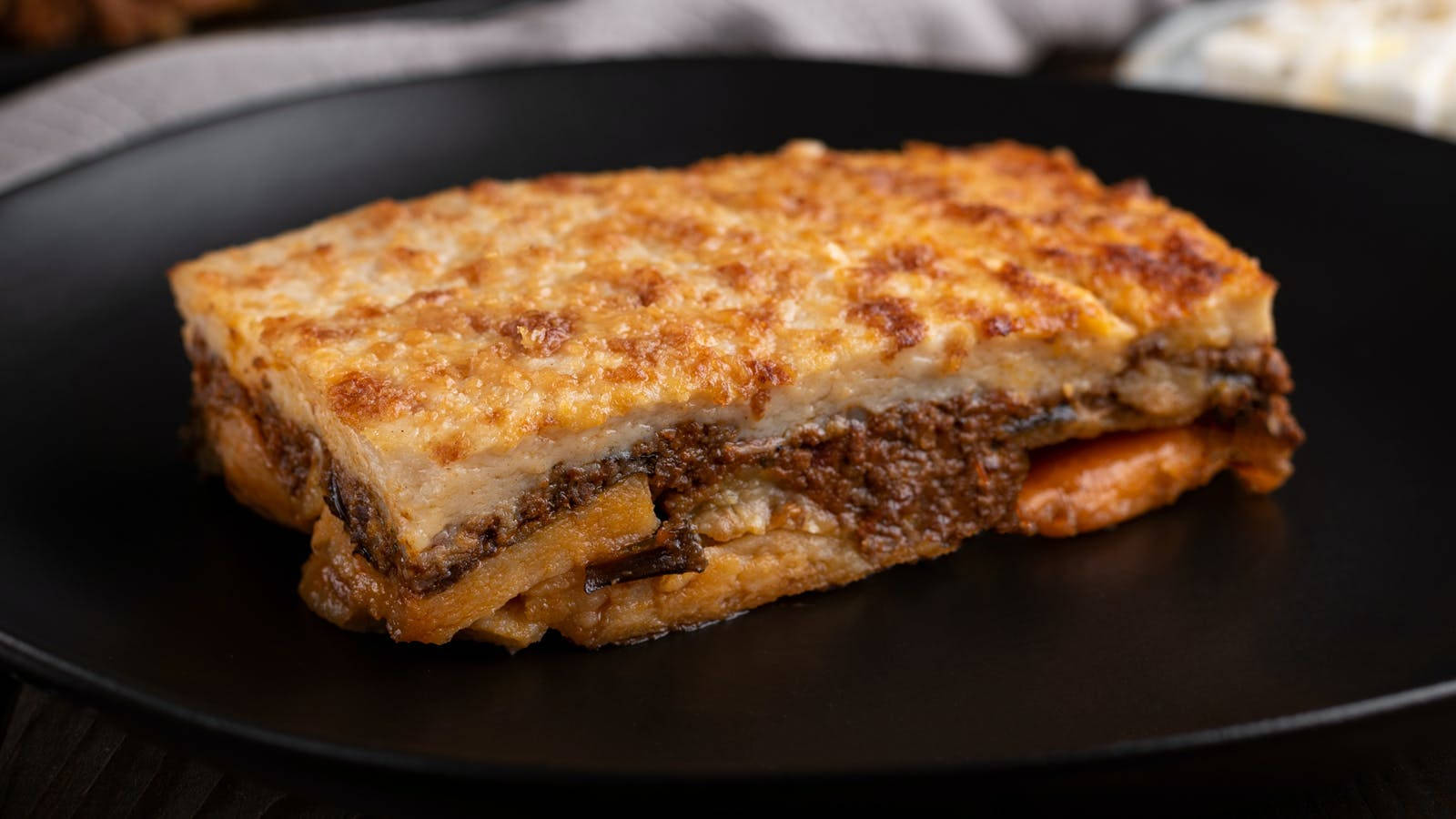 Slice Of Baked Moussaka On A Black Plate Background