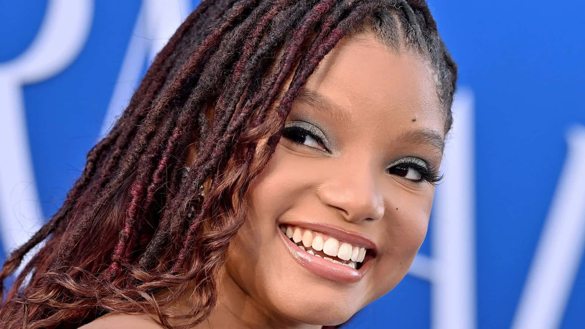 Smiling Celebritywith Braids Blue Backdrop Background