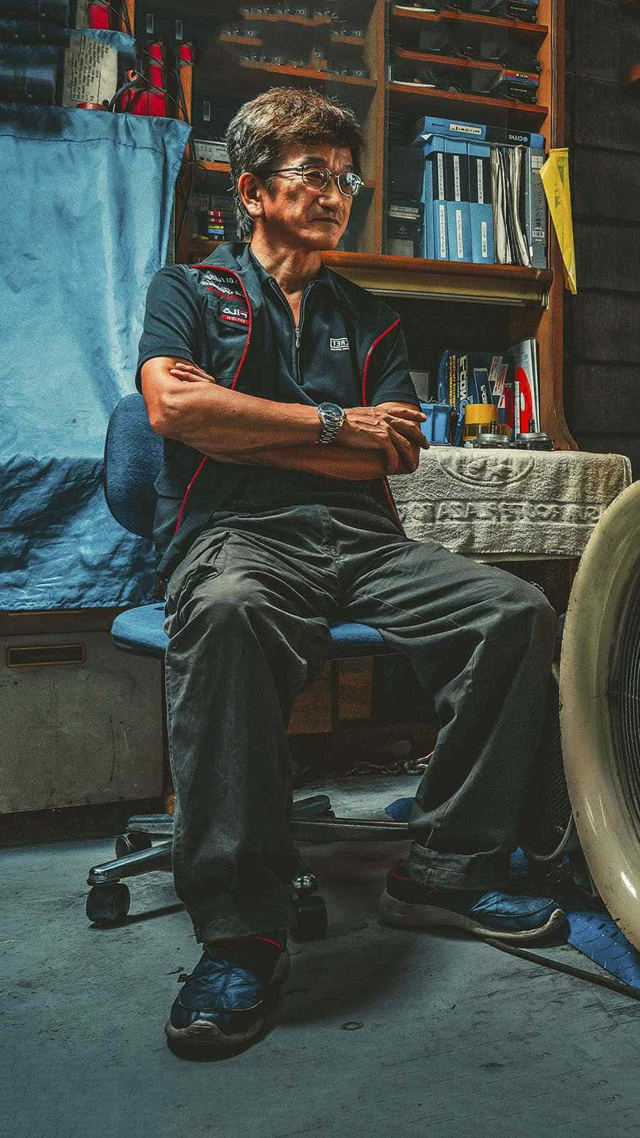 Smokey Nagata Sitting Inside A Repair Shop Background