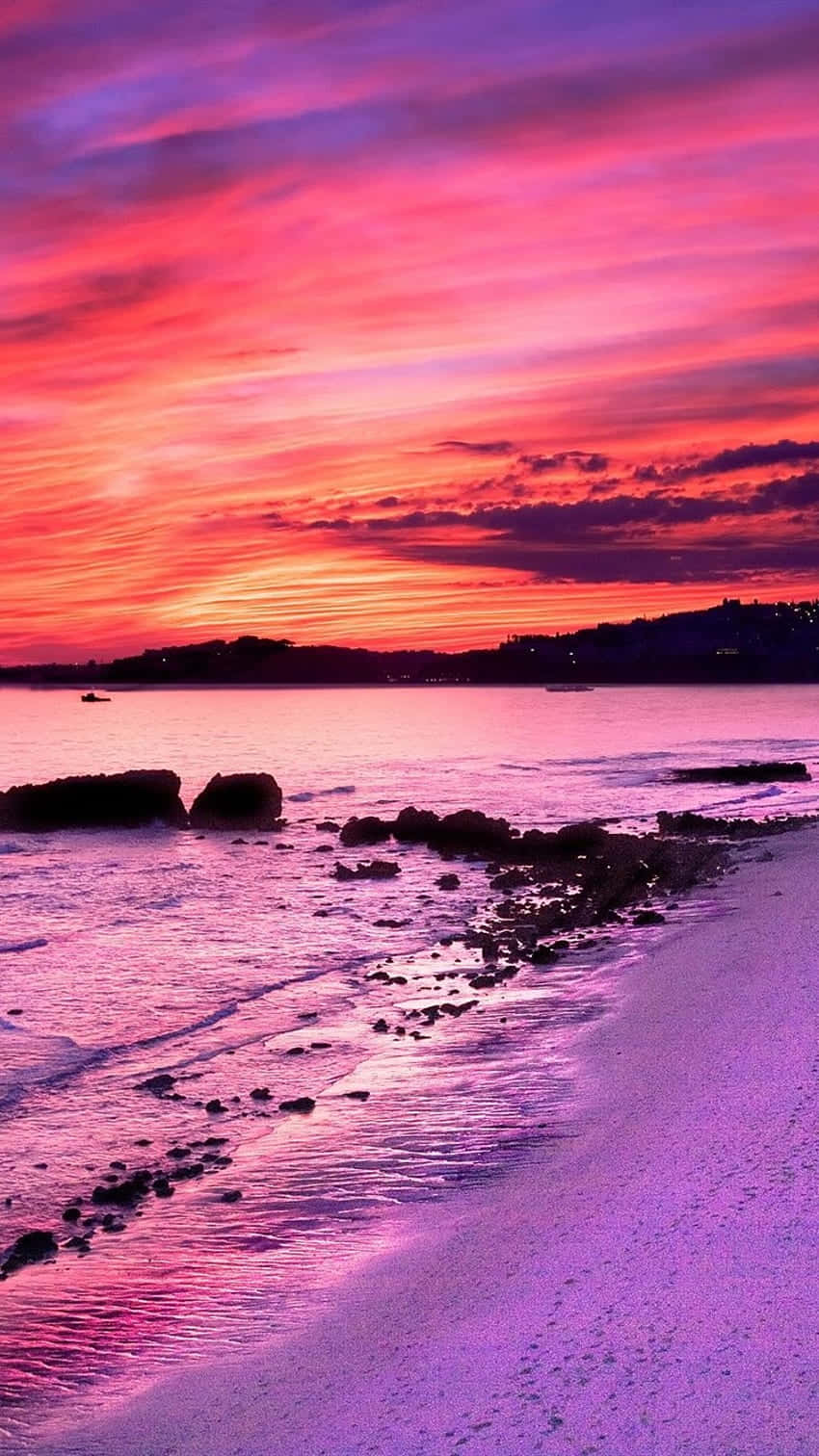 Soak In The Dreamy Pink Sunset With The Waves Lapping At Your Feet. Background