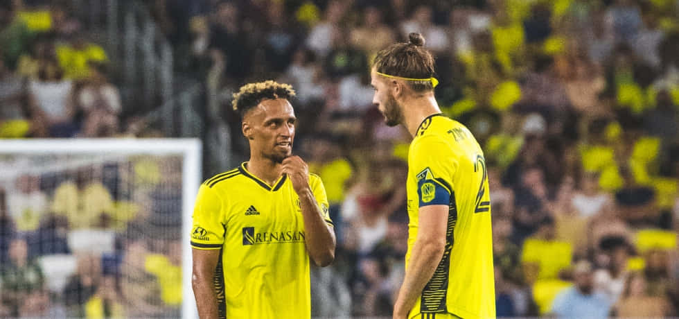 Soccer Players Discussing Strategy On Field Background