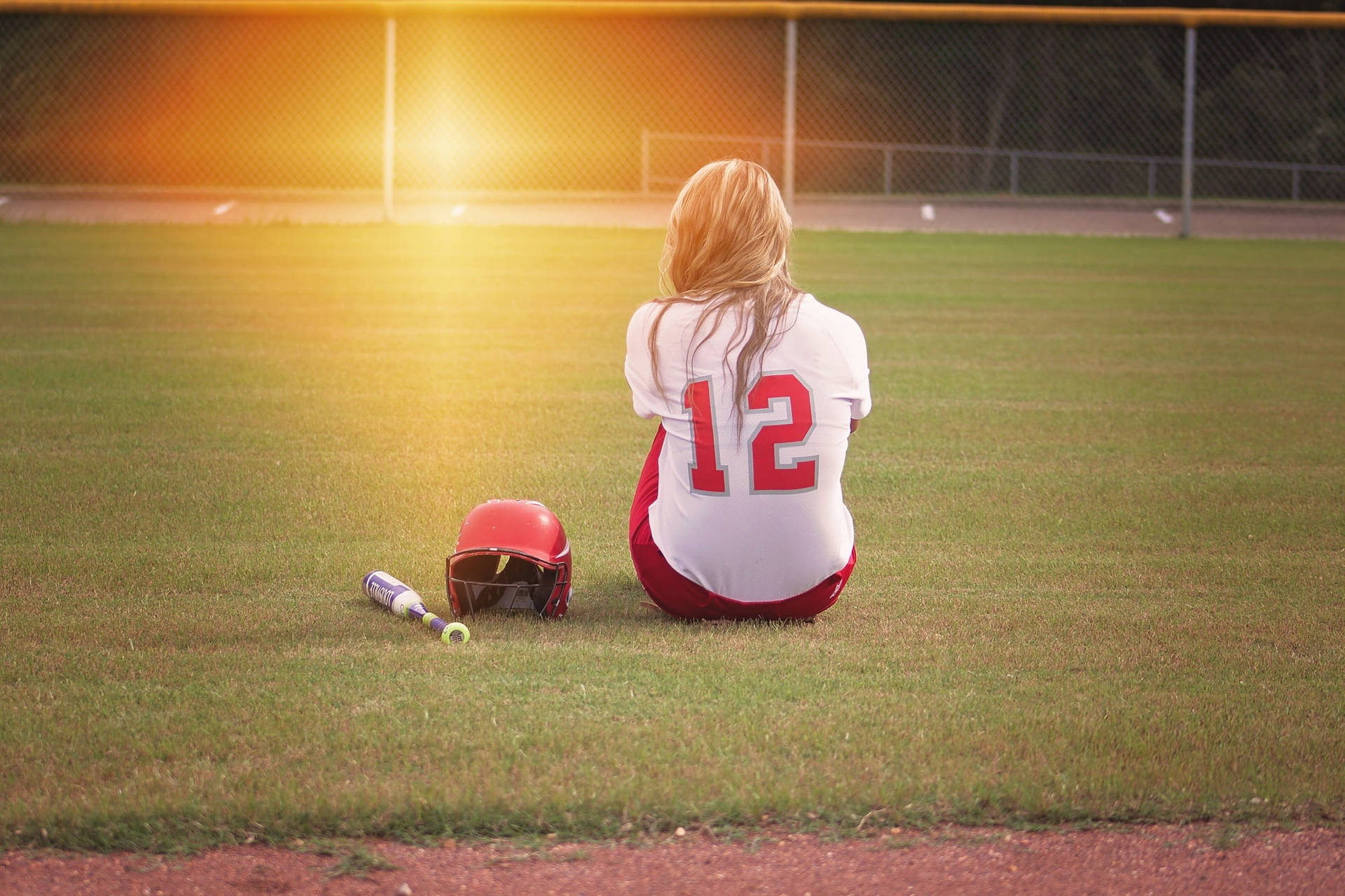 Softball Player Seated On Playing Field Background