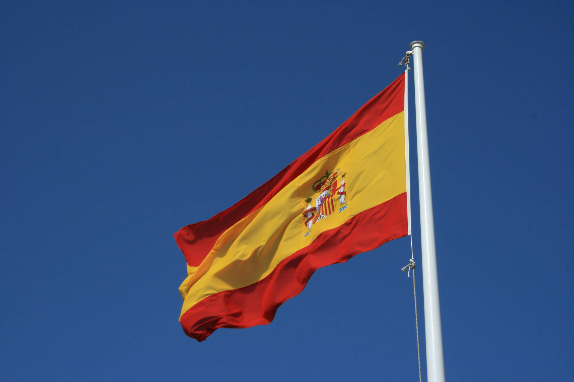 Spain's Pride - The Spanish Flag Majestically Flying Under Clear Blue Skies Background